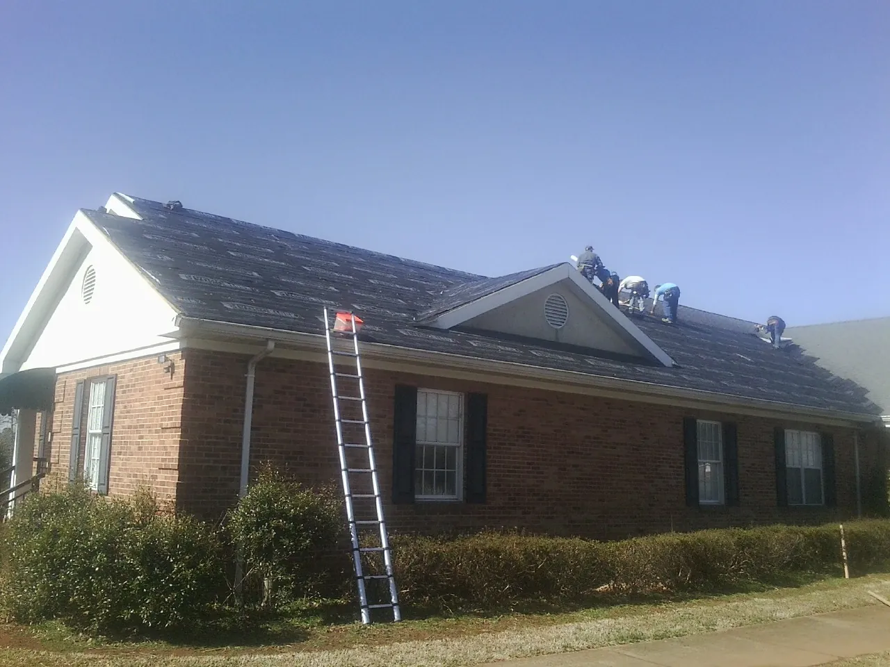 Crew tearing shingles off a brick ranch roof with a ladder set — Emergency Roof Repair work by our crew in Carnegie