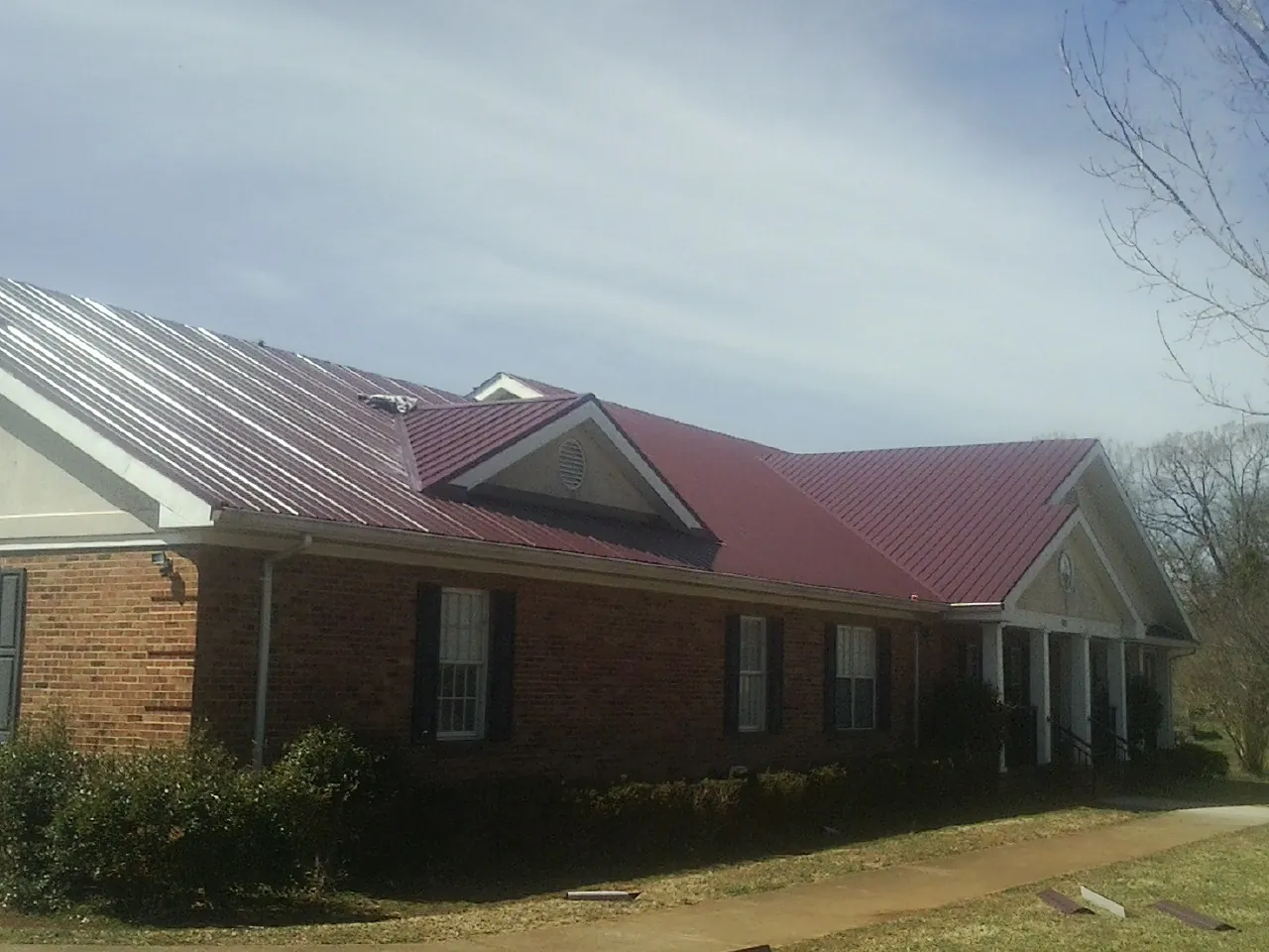 Red metal roof with gabled entries on a long brick building, from a Hail Damage Roof Repair job in Carnegie