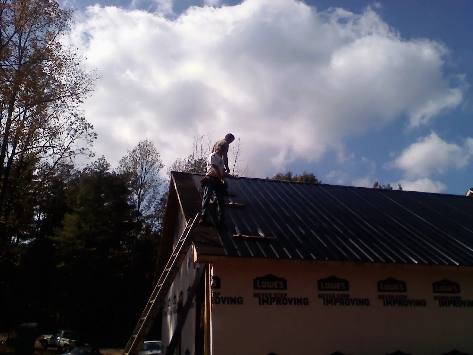 Roofer fastening dark metal panels high against a cloudy sky, from a Roof Inspection job in Carnegie